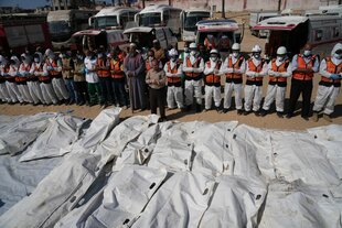 Medizinisches Personal steht vor einer Reihe weißer Leichensäcke und betet