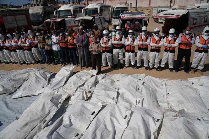 Medizinisches Personal steht vor einer Reihe weißer Leichensäcke und betet