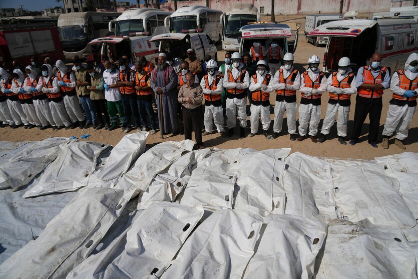 Medizinisches Personal steht vor einer Reihe weißer Leichensäcke und betet