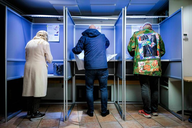 Drei Personen in Wahlkabinen von hinten