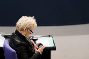Renate Künast sitzt im Deutschen Bundestag und blickt auf ihr Smartphone