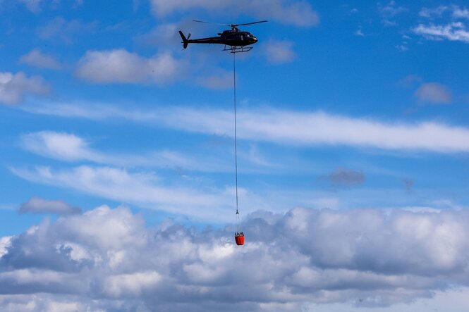 Ein Hubscheschrauber fliegt mit einem Wasserbehälter