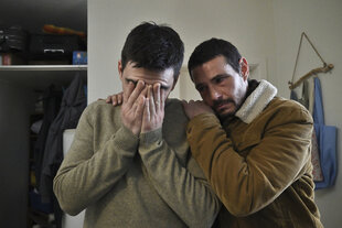 Ein Mann hält sein Gesicht in den Händen, ein Mann neben ihm tröstet ihn