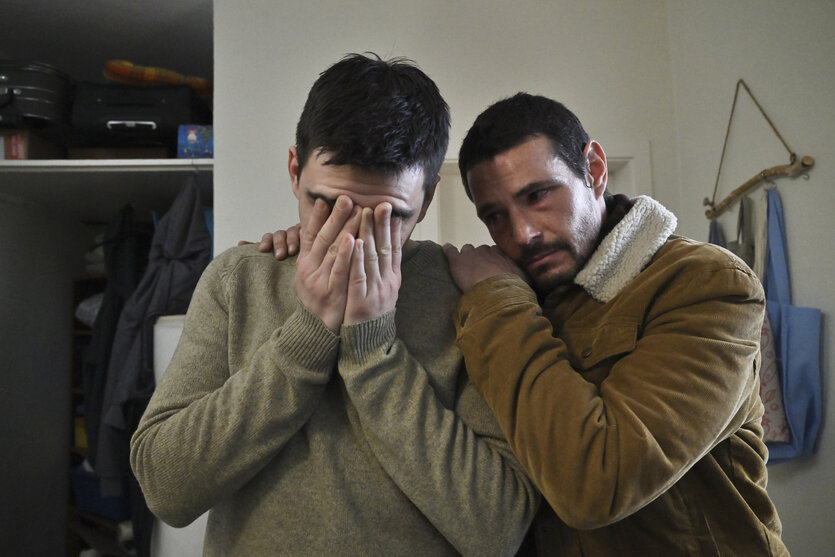 Ein Mann hält sein Gesicht in den Händen, ein Mann neben ihm tröstet ihn