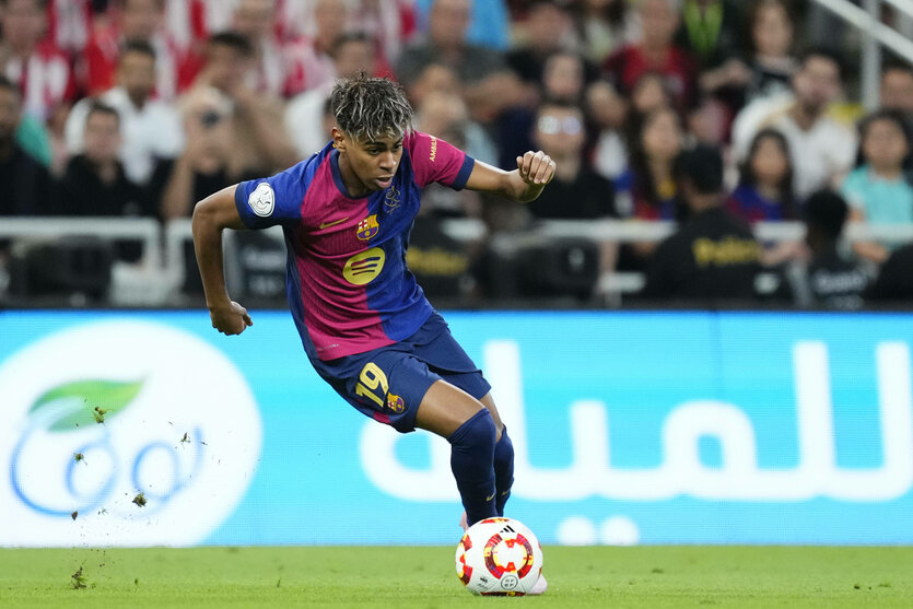 Lamine Yamal dribbelt mit dem Ball vor einer bandenwerbung in arabischer Schrift