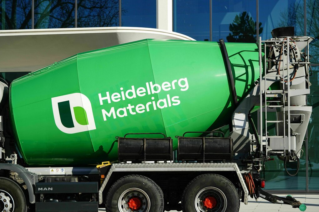 Ein Lkw mit grünem Betonmischer steht vor einer Glasfassade eines Bürogebäudes