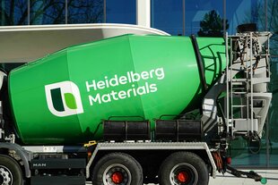 Ein Lkw mit grünem Betonmischer steht vor einer Glasfassade eines Bürogebäudes