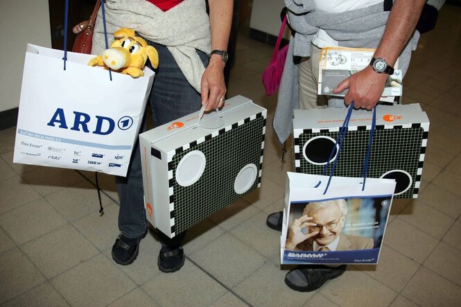 Menschen tragen PLastiktüten mit Werbeaufdrucken für ARD und ZDF