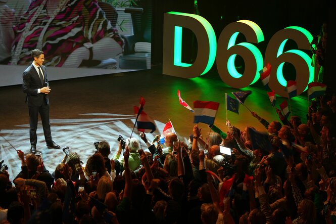 Rob Jetten steht auf einer Bühne vor jubelnden Anhängern mit Fähnchen, im Hintergrund das Logo „D66“