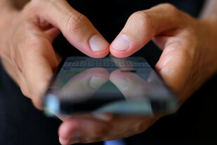 Jemand drückt mit zwei Daumen auf ein Smartphone