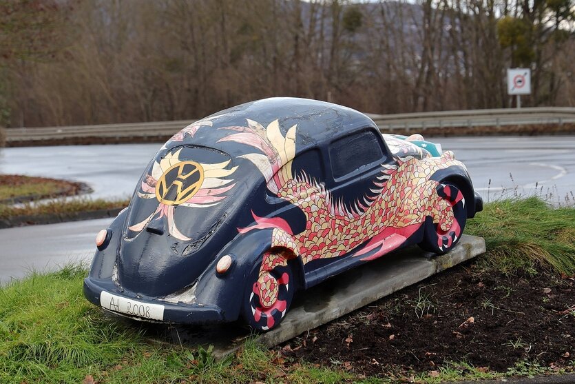 Ein VW Käfer ist bunt bemahlt und steht als Denkmal am Straßenrand