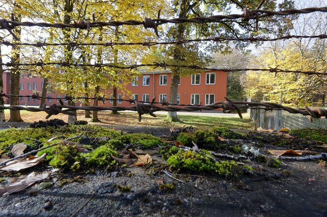 Blick durch einen Stacheldrahtzaun auf leerstehende Kasernengebäude
