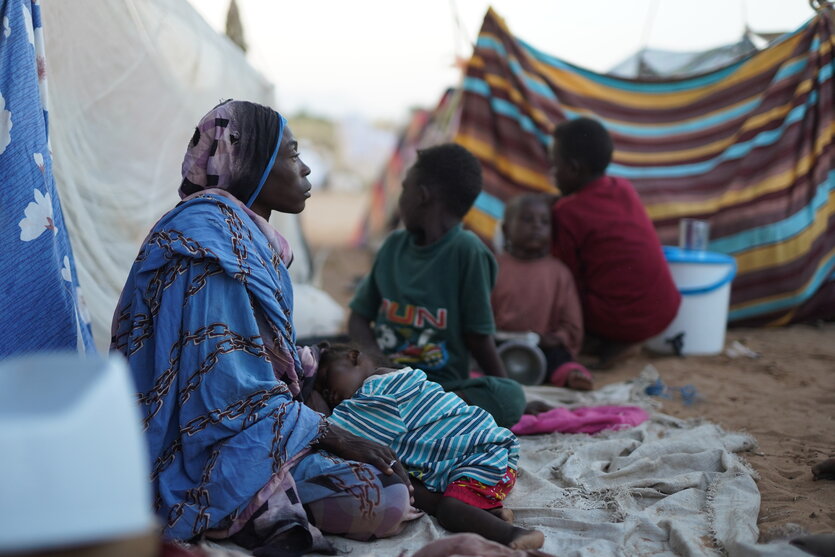 eine Frau in blauem Gewand sitzt mit Kindern auf dem Boden