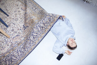 eine Frau liegt auf dem Boden und ist mit einem Teppich zugedeckt, neben ihr liegt ein Handy