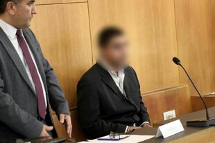 Ein Mann sitzt in einem Gerichtssaal, neben ihm steht ein Mann in Anzug