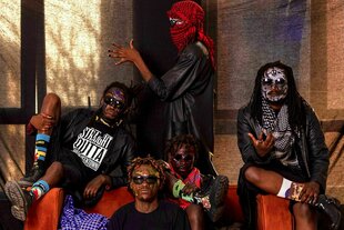 Die Band Chovu, bestehend aus vier schwarzn Personen, auf und um ein Sofa sitzende. Eine Person steht hinter dem Sofa mit rotem Keffiah zur Seite gedreht, zwei sitzen auf den Lehnen, eine sitzt auf der Couch und eine davor