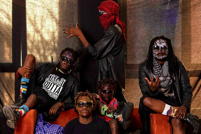 Die Band Chovu, bestehend aus vier schwarzn Personen, auf und um ein Sofa sitzende. Eine Person steht hinter dem Sofa mit rotem Keffiah zur Seite gedreht, zwei sitzen auf den Lehnen, eine sitzt auf der Couch und eine davor