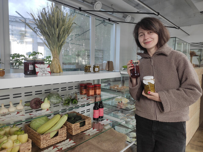 Eine Frau steht vor einer Verkaufstheke mit Gemüse, in der Hand hält sie zwei Einmachgläser
