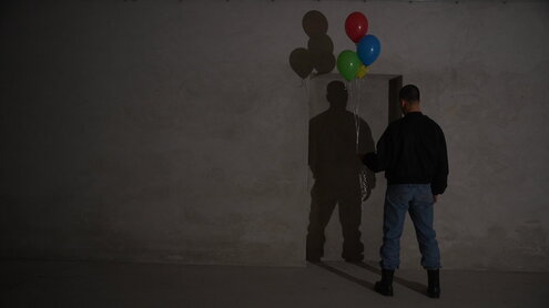 Ein Mann steht mit bunten Ballons vor einer grauen Wand
