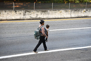Eine geflüchtete Frau auf einer Landstraße trägt ihr Kind vor der Brust
