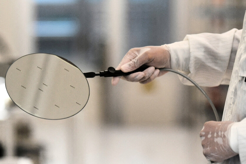 Ein Mensch in Schutzkleidung hät einen Wafer mit einer Pinzette