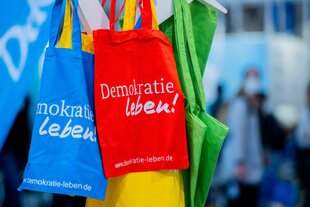 Blaue, rote und grüne Jutebeutel mit der Aufschrift "Demokratie leben"