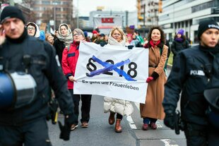 Eine Protestierende hält ein Banner, auf dem durchgestrischen steht: §218