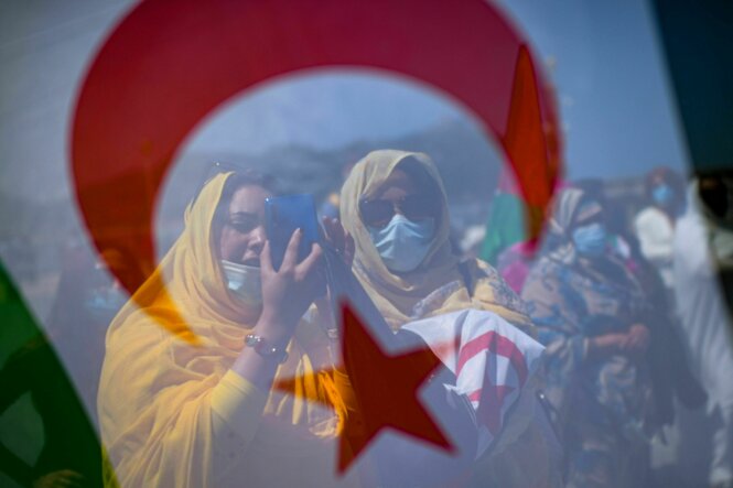 Demonstrantinnen stehen hinter einer Fahne der Westsahara. Eine Frau macht ein Foto.