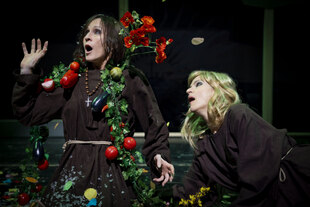 Zwei Schauspielerinnen in Franziskaner-Kutten mit Blumen und Gemüse