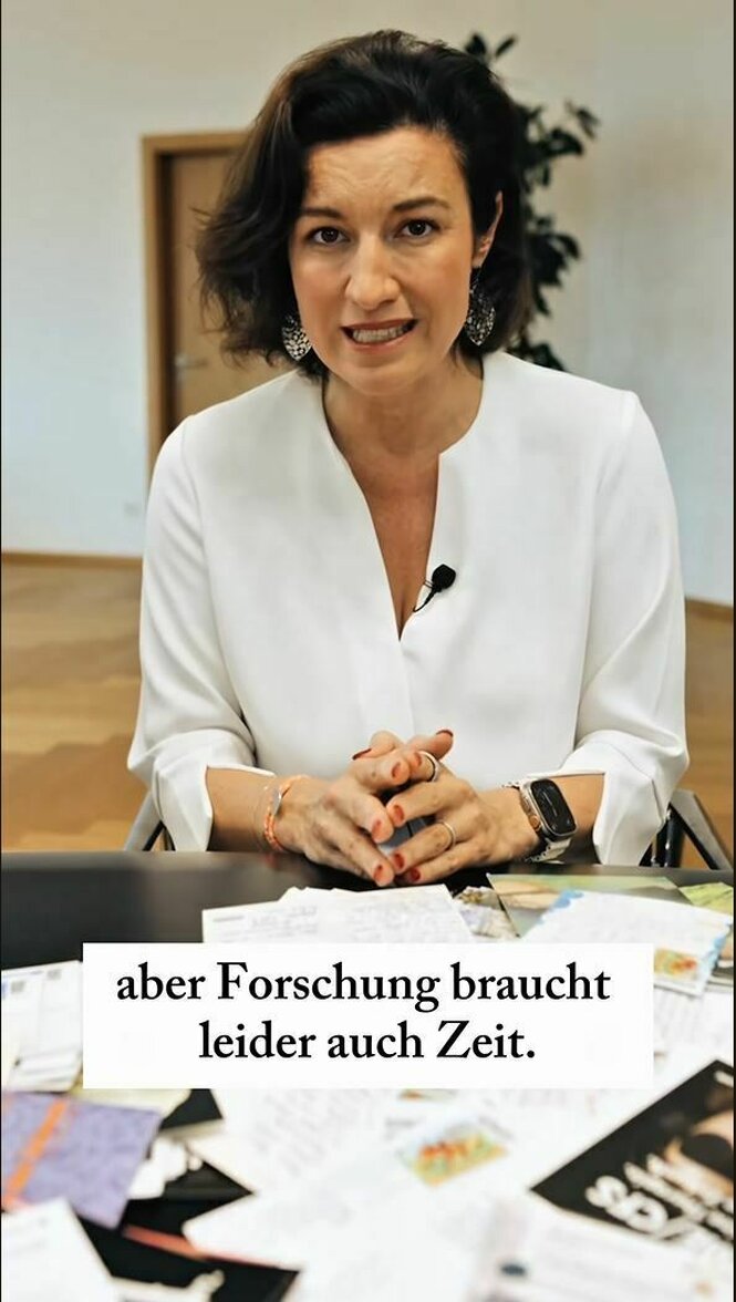 Dorothee Bär sitzt an einem Tisch, auf dem Briefe und Postkarten liegen, das Bild ist untertitelt mit dem Zitat: "aber Forschung braucht leider auch Zeit."