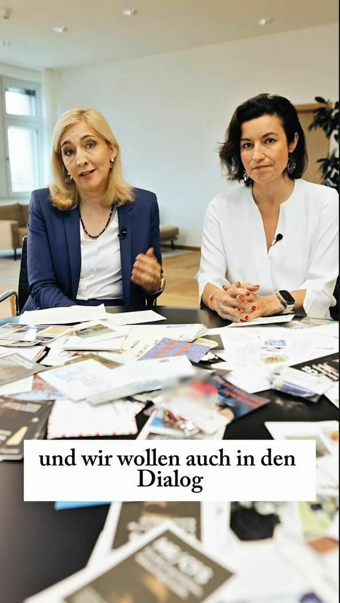Nina Warken und Dorothee Bär sitzen nebeneinander an einem Tisch, auf dem Briefe und Postkarten liegen, das Bild ist untertitelt mit dem Zitat: "und wir wollen auch in den Dialog"