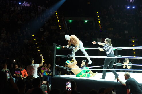 Ein maskierter Mann steigt mit dem rechten Fuß auf den am Boden liegenden Kontrahenten im Ring