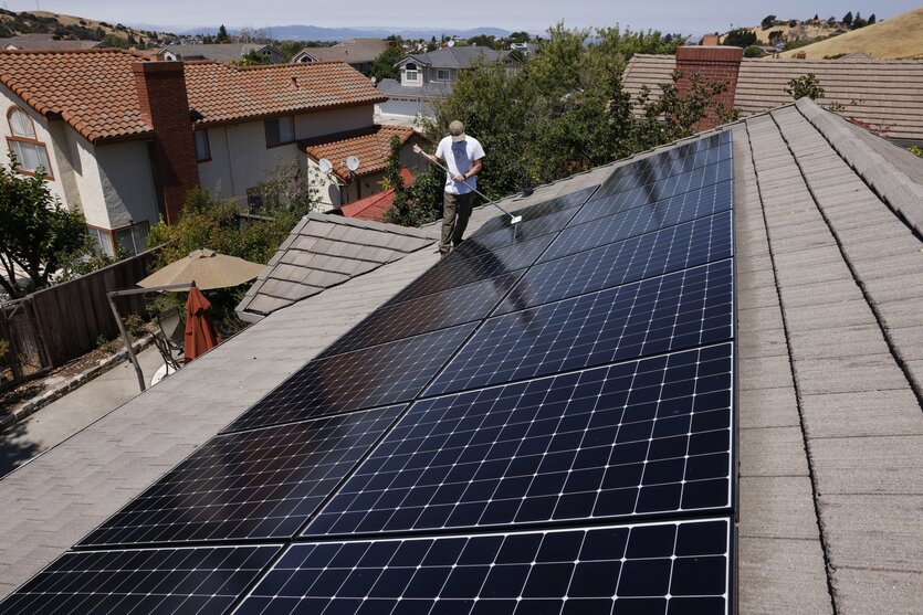 Ein Mann reinigt eine Solaranlage, die auf dem Dach eines Wohnhauses installiert ist.