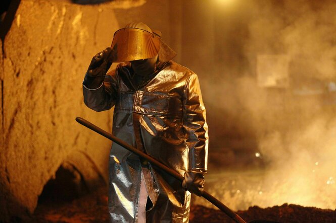 Ein Stahlarbeiter in Schutzkleidung steht vor einem Hochofen