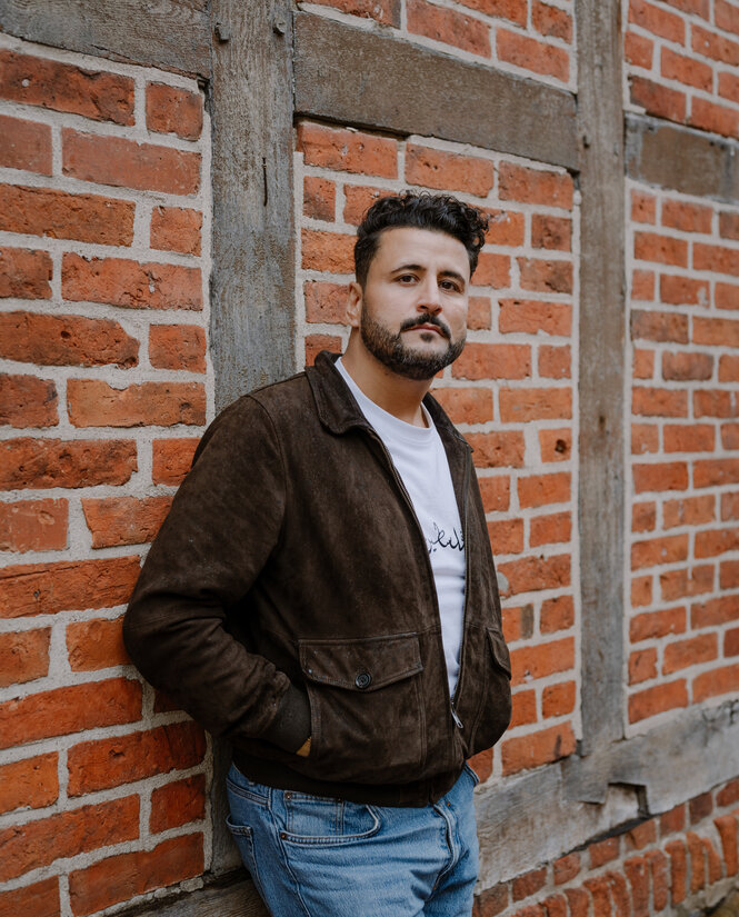 Ein Mann lehnt an einer Häuserwand