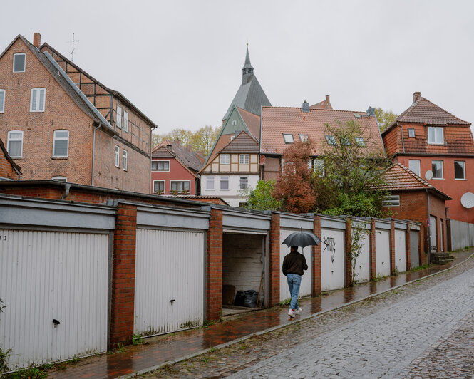 Ein Mann mit Regenschirm läuft an Garagen vorbei