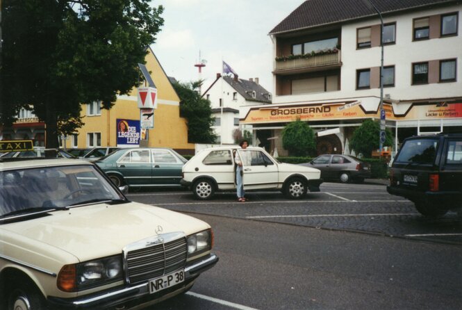 Eine Person an einem Auto auf einem Dorfplatz.