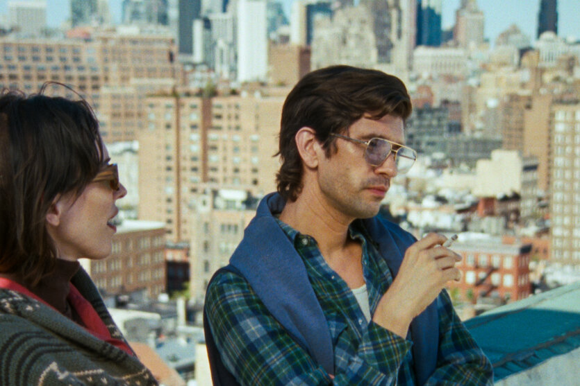 Szene aus dem Film, in der Linda Rosenkrantz, gespielt von Rebecca Hall, und Peter Hujar, gespielt von Ben Whishaw, rauchend auf der Dachterasse vor der New Yorker Skyline stehen