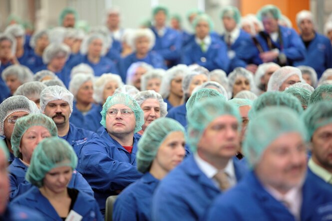 Viele Beschäftigte in Schutzkleidung sitzen in einem Raum