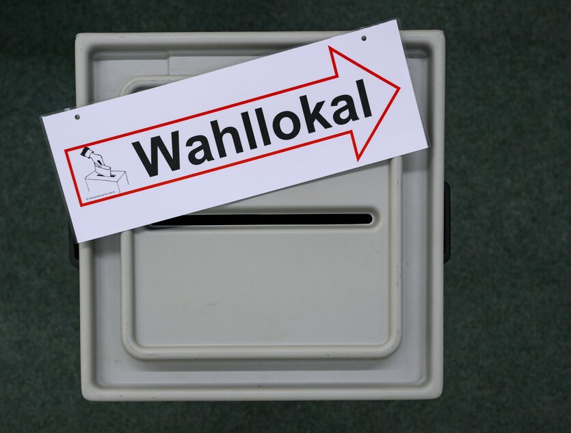 Das Bild zegt den Einwurfschlitz einer Wahlurne, auf der ein Schild mit der Aufschrift "Wahllokal" liegt.