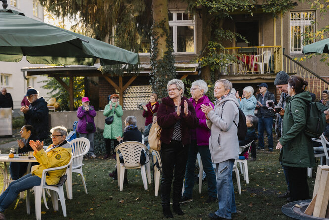 Senior*innen stehen im Garten eines Hauses bei einer Feier