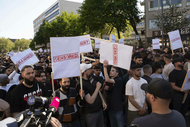 Eine Menschenmenge demsnstriert mit Schildern, auf denen 