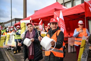 Frauen streiken, sie tragen Arbeitskleidung und trommeln auf Eimern