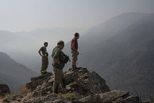 Drei Männer stehen in einer dunstigen Berglandschaft und schauen ins Tal