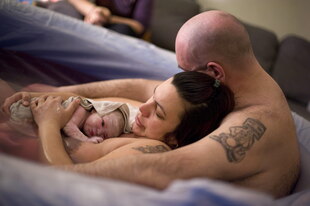 Eine Familie kuschelt mit einem frisch geborenem Baby in einer Geburtswanne