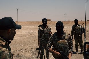 Vermummte Männer in Soldatenuniformen stehen in einer Wüstenlandschaft