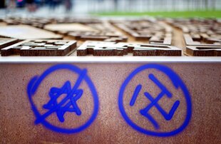 Mit Graffiti sind ein Davidstern und ein Hakenkreuz an eine Mauer gesprayt. Der Davidstern ist durchgestrichen.