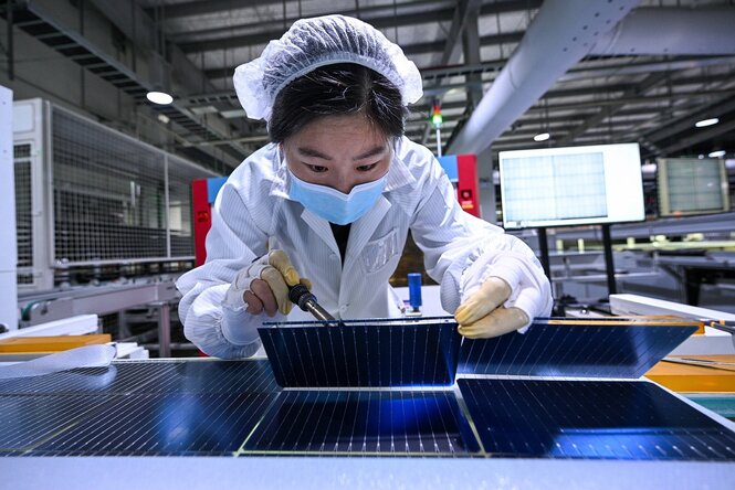 Eine Frau mit Mundschutzmaske arbeitet in einer Produktionsanlage für Solarmodule