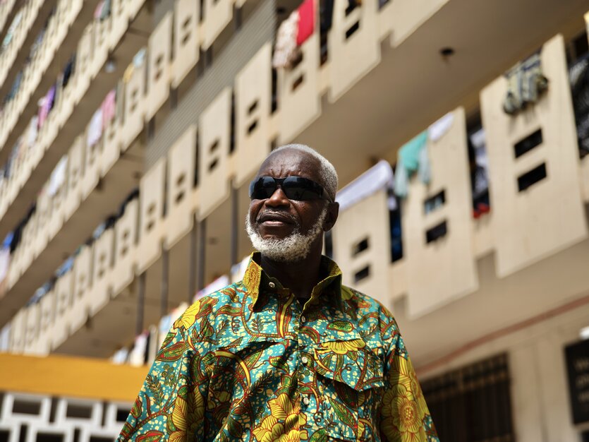 Ein Mann mit Sonnenbrille und buntem Hemd vor einer Häuserwand