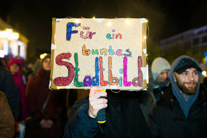 Auf einem Schild bei einer nächtlichen Demonstration steht: "Für ein buntes Stadtbild"
